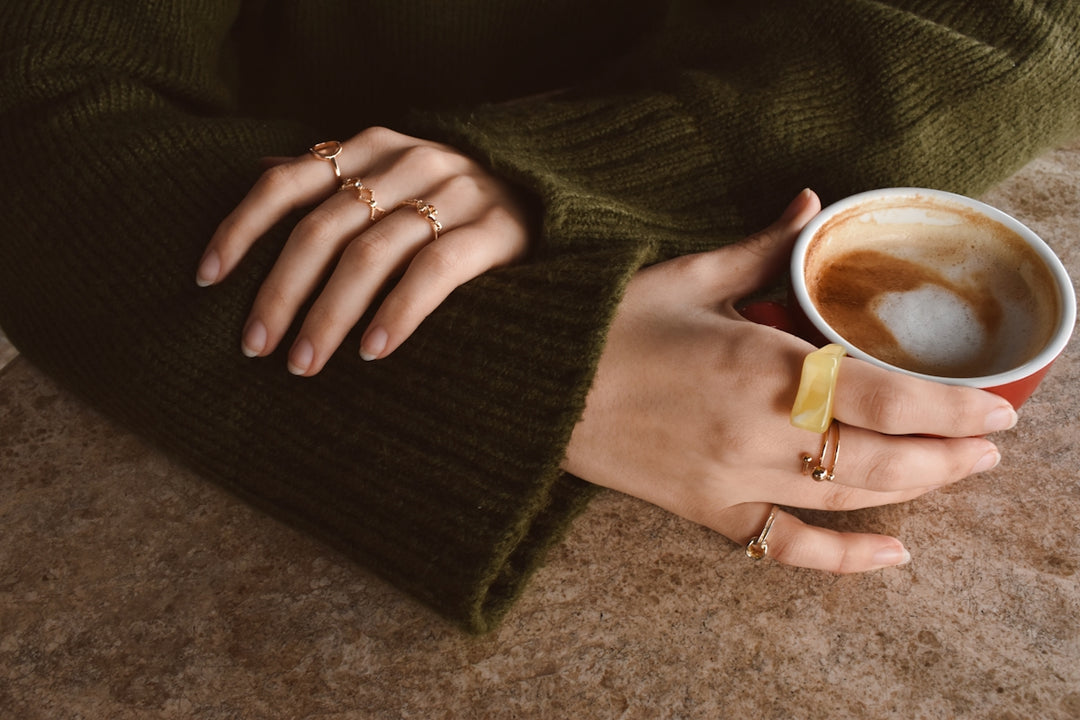 Hands wearing rings holding a cup of coffee.